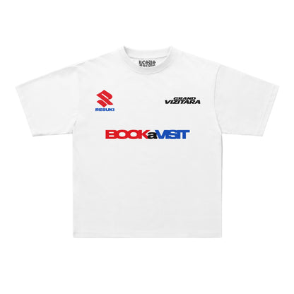A white short-sleeve crewneck t-shirt featuring sponsor logos on the chest, including the red and blue Suzuki logo, the black 'Grand Viztara' text, and the red and blue 'BookaMST' logo. The shirt is displayed flat against a clean, light off-white background.