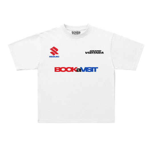 A white short-sleeve crewneck t-shirt featuring sponsor logos on the chest, including the red and blue Suzuki logo, the black 'Grand Viztara' text, and the red and blue 'BookaMST' logo. The shirt is displayed flat against a clean, light off-white background.