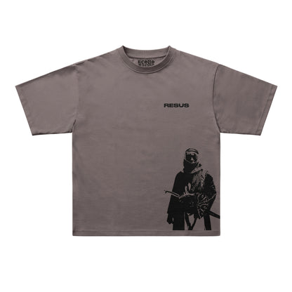 A taupe gray short-sleeve t-shirt with a black graphic print of a masked soldier on the lower right and the word 'RESUS' printed on the upper chest. The brand 'UNIQUELY AVAILABLE' is visible inside the collar.