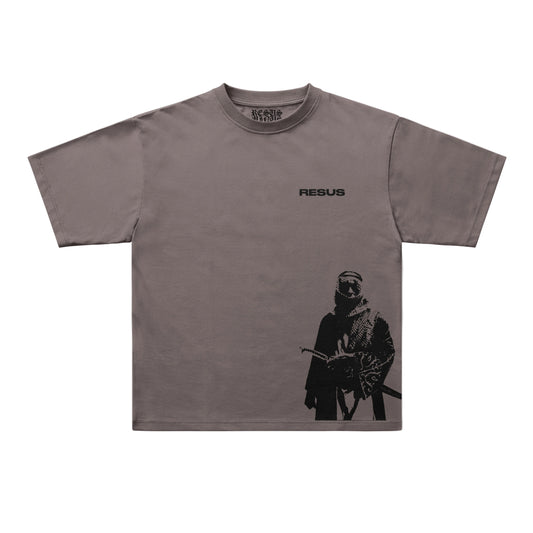 A taupe gray short-sleeve t-shirt with a black graphic print of a masked soldier on the lower right and the word 'RESUS' printed on the upper chest. The brand 'UNIQUELY AVAILABLE' is visible inside the collar.